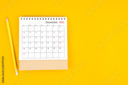 December 2023 desk calendar and wooden pencil on yellow color background.