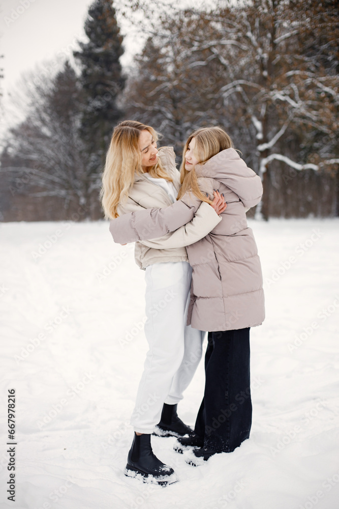 Portrait of blonde mother and teen daughter standing in winter forest