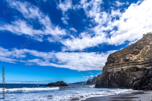 Beach with black volcanic sand, green palm trees on the slope, dangerous waves, Atlantic Ocean, Castro Beach © dominikspalek.pl