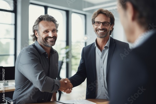 Smiling middle aged business man handshaking partner, making partnership collaboration agreement at office meeting. HR manager and new worker shake hands recruiting at job interview.  photo