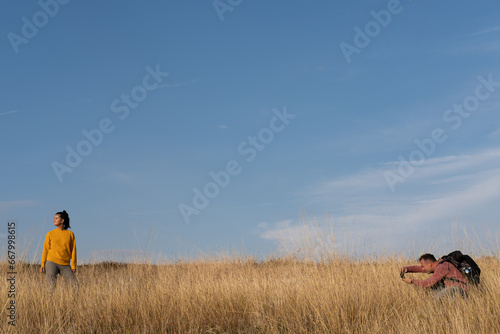Man taking photo of a woman in the autumn field against blue sky during warm sunny day. Weekend, leisure, relationship activities