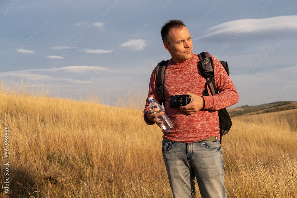 Young man hiking through autumn fields and hills against blue sky during warm day and photographing nature. Weekend, leisure, sport