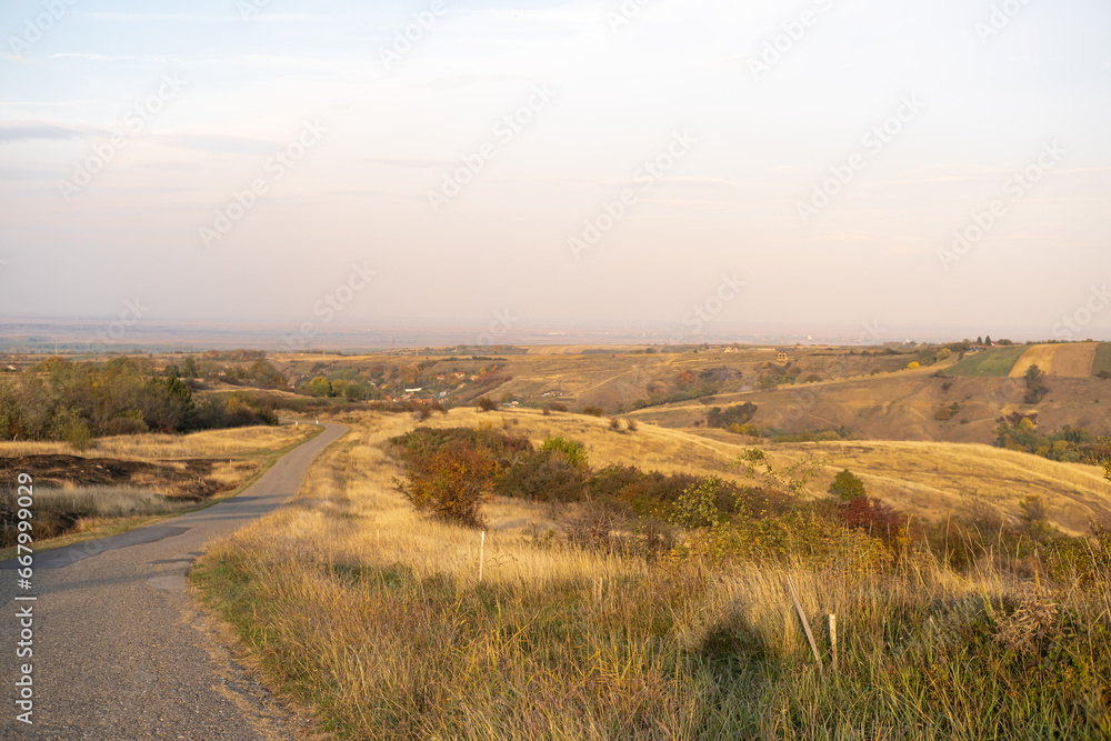 Beautiful autumn rural landscape. Countryside mountain scenery with empty road at sunset. Fields and meadow on rolling hills with golden light.