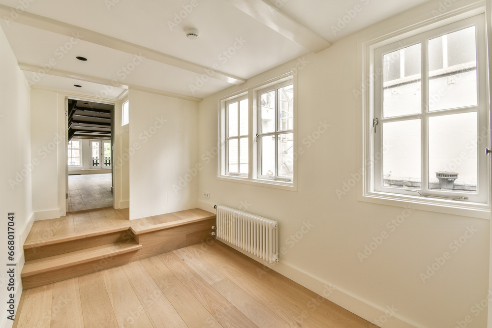 an empty room with white walls and wood flooring on the right, there is a window to the left an empty room with white walls and wood flooring on the right, there is a window to the left