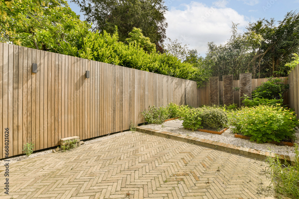 a backyard with a wooden fence and brick path leading to the back yard, surrounded by lush green trees on a blue sky background a backyard with a wooden fence and brick path leading to the back yard, surrounded by lush green trees on a blue sky background