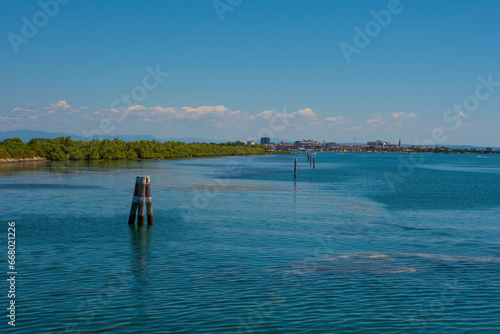 Markers show the edge of a navigable channel in the shallow waters in the Grado section of the Marano and Grado Lagoon in Friuli-Venezia Giulia  north east Italy. August. Grado town is seen in the bac