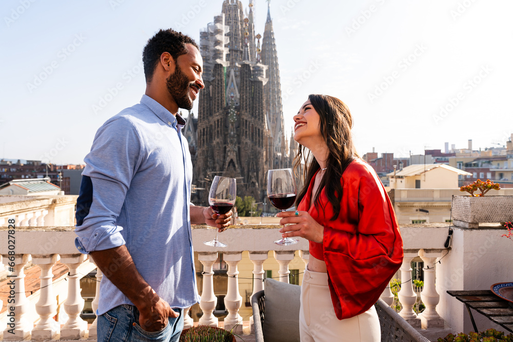 Multiracial beautiful happy couple of lovers dating on rooftop balcony at Sagrada Familia, Barcelona - Multiethnic people having romantic aperitif on a terrace with city view , concept about tourism - obrazy, fototapety, plakaty 