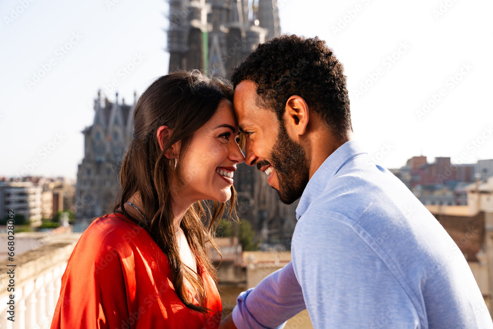 Multiracial beautiful happy couple of lovers dating on rooftop balcony at Sagrada Familia, Barcelona - Multiethnic people having romantic meeting on a terrace with city view , concept about tourism 