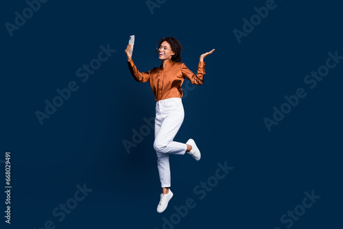 Full size photo of pretty young girl selfie jump video call dressed stylish brown silk formalwear isolated on dark blue color background
