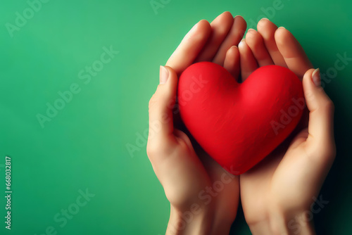 hands hold a red heart on a green background