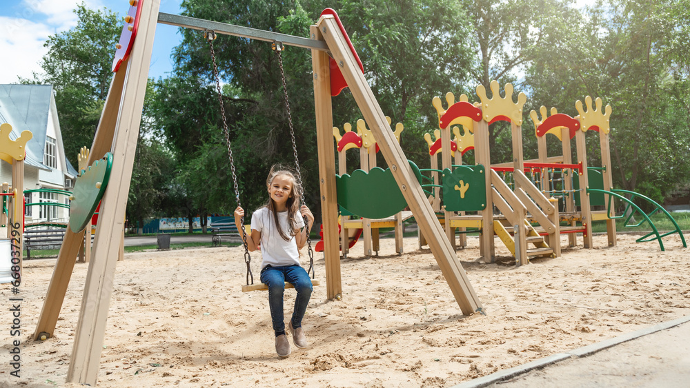 The child plays in the outdoor playground. Active little girl swings on a colorful swing. Healthy summer activity for kids. The child plays in the outdoor playground. Active little girl swings on a colorful swing. Healthy summer activity for kids.