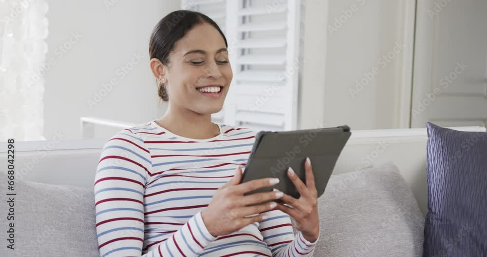 Happy biracial woman sitting on sofa using tablet, slow motion Happy biracial woman sitting on sofa using tablet, slow motion