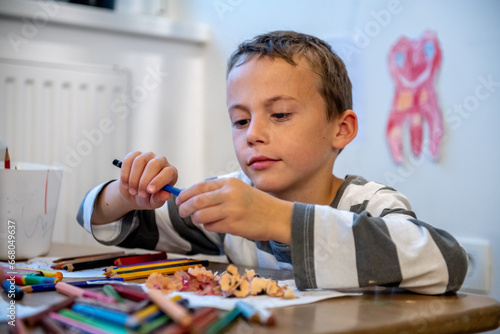 child preparing for schoolwork. the boy sewing crayons. he is sitting bihind floor sitting desk.