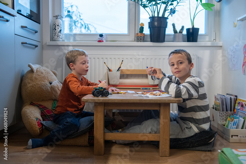 two children draw with crayons. they are sitting at the table. They are getting ready for school.