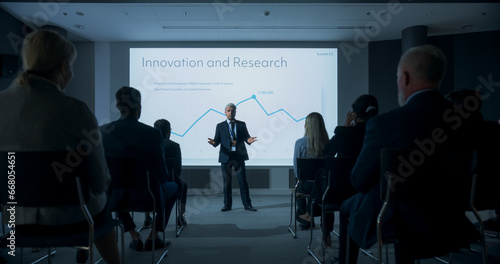Corporate Event: Caucasian Male Tech CEO Giving Presentation To Colleagues or Investors In the Conference Room Of Innovative Startup Office. Man Talking About Business Objectives and Profit Margins.