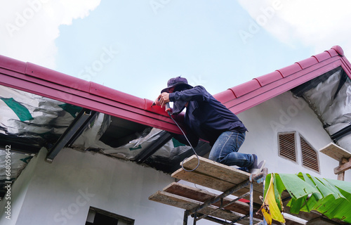 Construction man worker using auger to attach roofer.Roofing installation and building new house exterior.Roofer Install, repair on the rooftop outdoor.Home improvement, renovation concept.