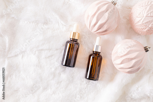 Two cosmetic bottles with dropper with natural self-care product on white fur background with elegant christmas balls. A copy of the space.