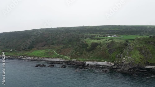 Aerial dolly forward shot of the Gobbins Cliffs in Northern Ireland during an adventurous journey overlooking the coast road, calm sea and rocks on a cloudy morning on an expedition photo