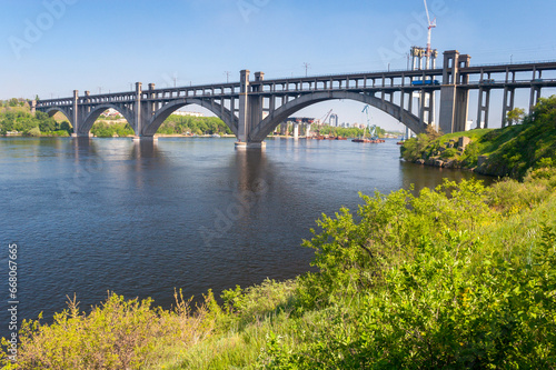 Preobrazhensky concrete arched bridge on Dnieper river in spring, view from Khortytsia island, Zaporizhzhia, Ukraine