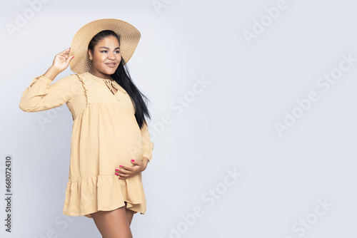A pregnant African-American woman, in a dress, on a light background.
