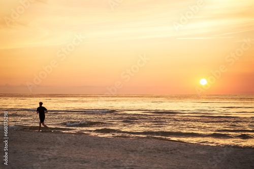 Silhouette of a sportsman running near the ocean shore at sunset.