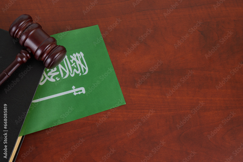 Saudi Arabia legal and law concept, judge gavel with book on table and Saudi Arabia flag.  The Arabic inscription on the flag: 