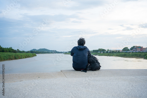 asian man sit and relax at side of river during sunset