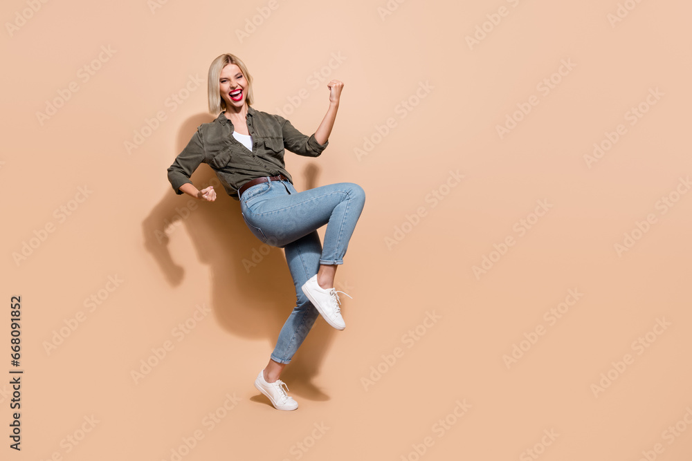 Full length photo of astonished lady succeeded work raise leg yell hooray wear trendy clothes isolated beige color background Full length photo of astonished lady succeeded work raise leg yell hooray wear trendy clothes isolated beige color background