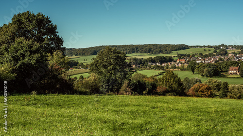 Lush hilly countryside with village on hillside under a blue sky during summer.