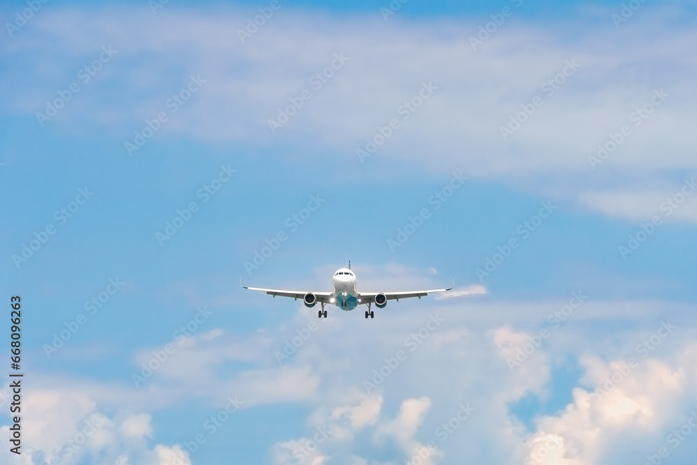 Close-up of a passenger plane with its headlights on is landing against a background of blue sky with clouds. Concept of a fast way to travel on vacation, business. Travel by air