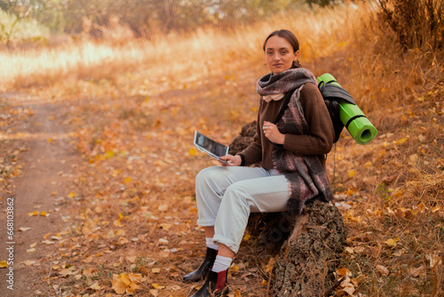 girl with a backpack and a map in the forest, sitting on a log, looking at a map in the autumn forest, autumn holidays and hiking, lifestyle concept