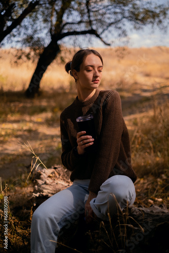 young woman relaxing outdoors on an autumn day  traveling to the forest  sitting on a wooden log in the forest and drinking hot tea  unity with nature  searching for the meaning of life