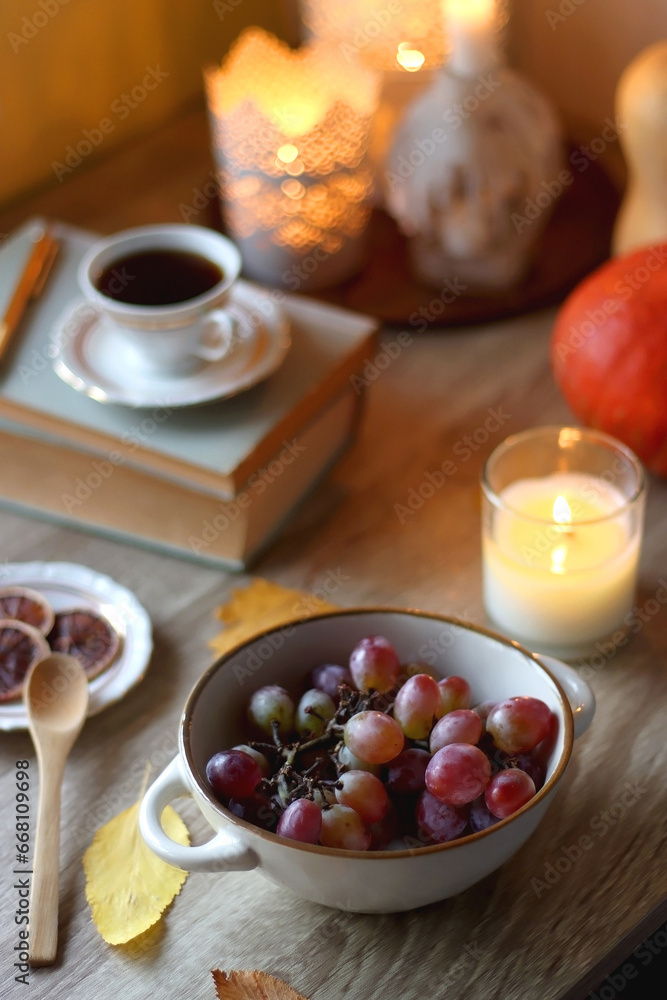 Cup of tea or coffee, plate with desserts, dried oranges, bowl of grapes, scented candles, vintage books, pumpkins and autumn leaves on the table. Autumnal hygge. Selective focus. Cup of tea or coffee, plate with desserts, dried oranges, bowl of grapes, scented candles, vintage books, pumpkins and autumn leaves on the table. Autumnal hygge. Selective focus.