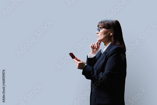 Mature business woman with smartphone, profile view on grey background