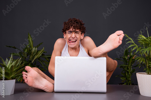 A funny young man sits at a laptop with his feet up on the table. Watching videos for adults. Dating on the Internet. photo