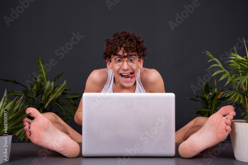A funny young man sits at a laptop with his feet up on the table. Watching videos for adults. Dating on the Internet.