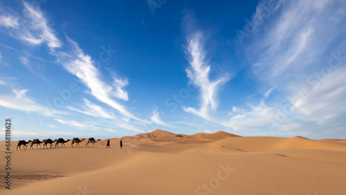 Two unidentified Berber men leading a camel caravan across sand dunes in Sahara Desert, Morocco