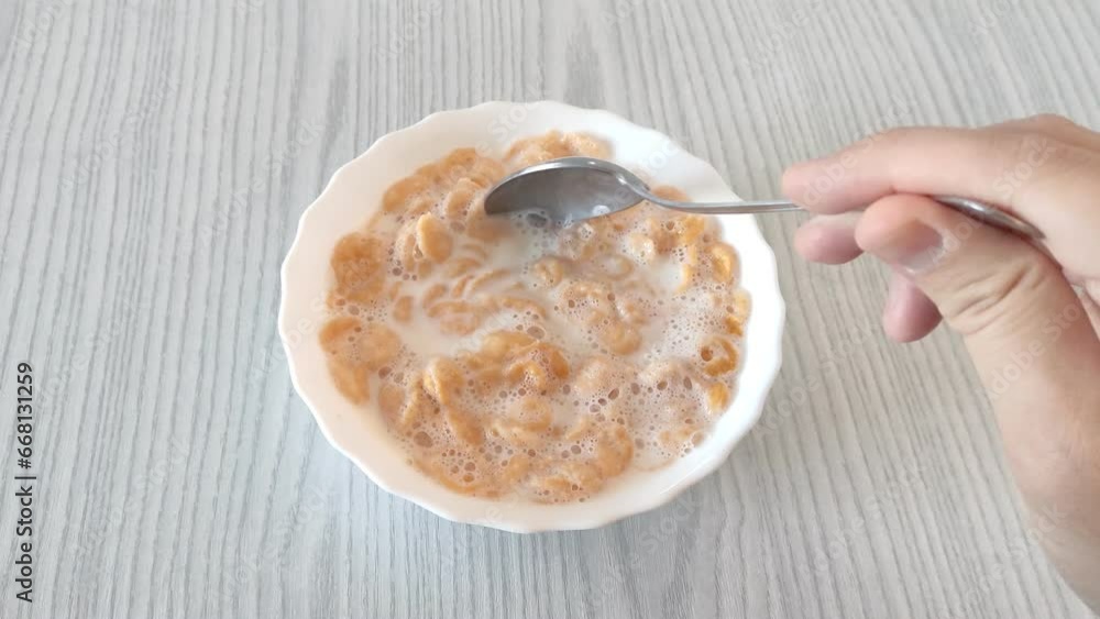 Man stirs cornflakes with milk in a plate with a spoon Man stirs cornflakes with milk in a plate with a spoon
