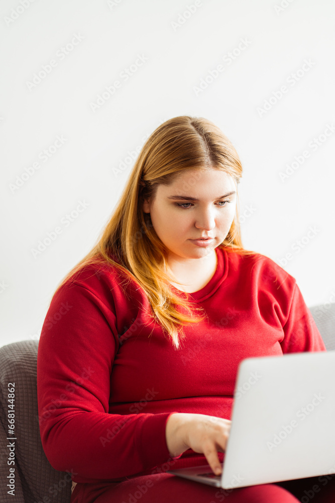 Portrait of serious plus size woman using laptop, sitting on comfortable sofa in living room at home Portrait of serious plus size woman using laptop, sitting on comfortable sofa in living room at home