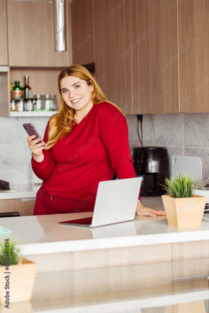 Smiling beautiful plus size woman wearing red casual clothes holding mobile phone, using laptop Smiling beautiful plus size woman wearing red casual clothes holding mobile phone, using laptop