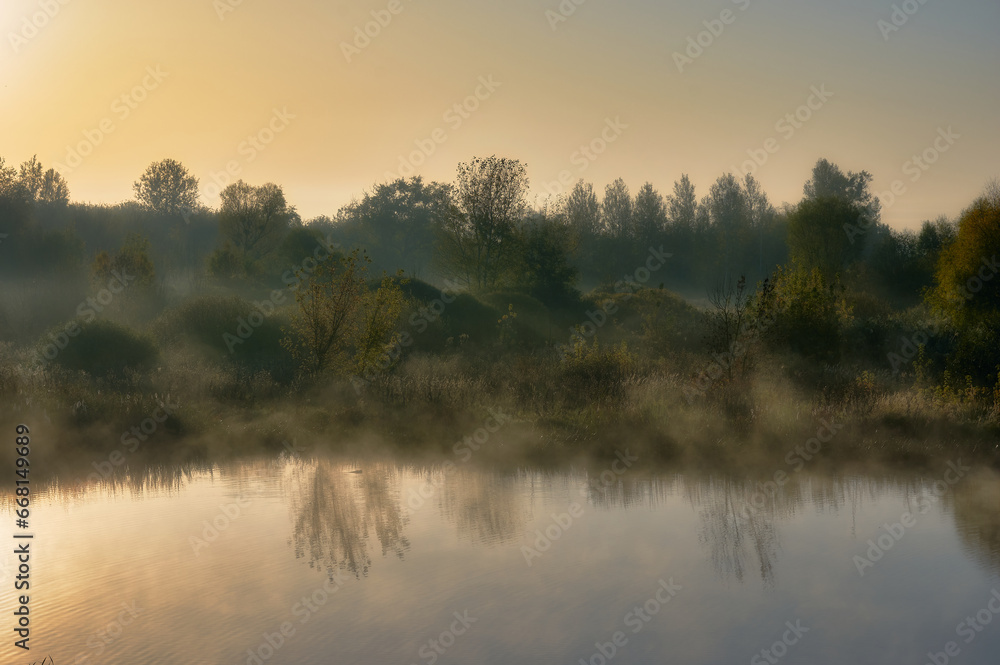 Early autumn morning, light fog swirls on the surface of the lake, clear sky and dense bushes on the shore, autumn mood
