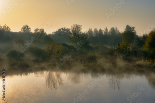 Early autumn morning, light fog swirls on the surface of the lake, clear sky and dense bushes on the shore, autumn mood