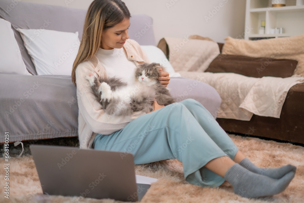 White woman sitting on floor carrying her Persian cat on her lap touching her own cat with love, while while working relationship with human and pet concept. White woman sitting on floor carrying her Persian cat on her lap touching her own cat with love, while while working relationship with human and pet concept.