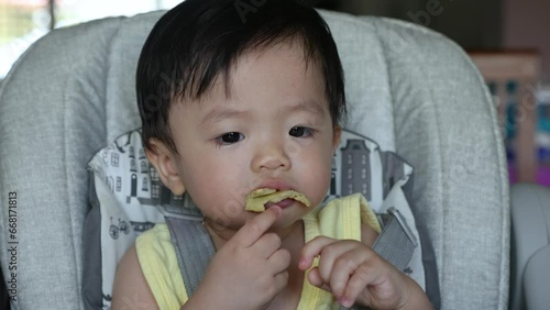 Happy 1years old Chinese baby boy having food while sit on baby chair photo