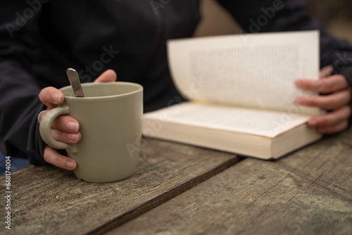 Glamping exterior, close-up detail of a woman's hands holding a cup of coffee while reading a book.