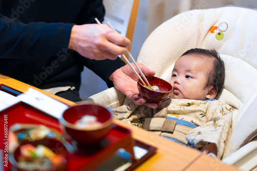 Fotografie 生後100日のお食い初めでパパにもらうご飯を不思議そうに見つめる生後3か月の赤ちゃん