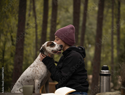 Chica con sombrero de invierno está sentado y acariciando a su perro están al aire libre