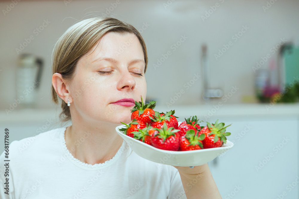 Woman smelling ripe red strawberries on white plate. Concept of eating natural sugar products and stay healthy and thin. Dieting concept, raw fruits diet Woman smelling ripe red strawberries on white plate. Concept of eating natural sugar products and stay healthy and thin. Dieting concept, raw fruits diet