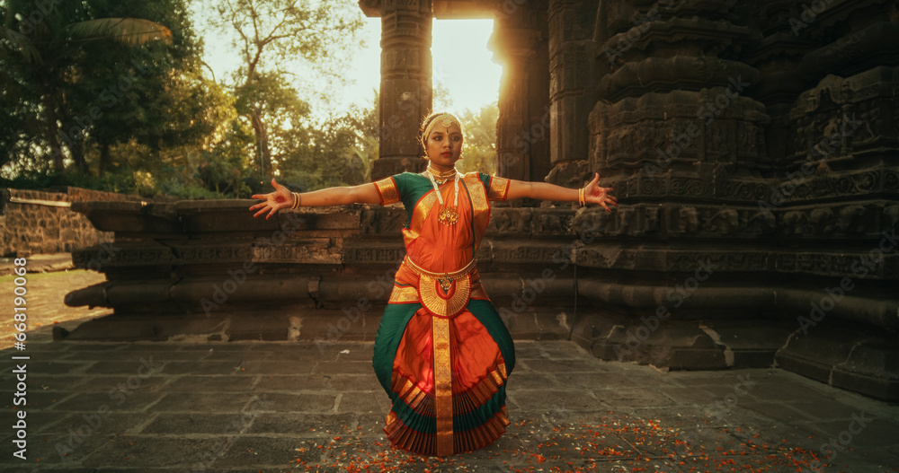 Dynamic Shot of Indian Woman in Traditional Clothes Dancing Bharatanatyam in Colourful Sari While Looking at the Camera. Expressive Young Female Performing Folk Dance Choreography in a Temple