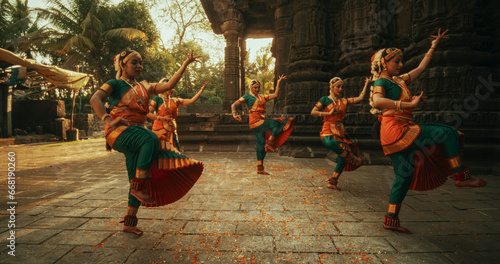 Fotografie Dynamic Shot of Indian Women in Traditional Clothes Dancing Bharatanatyam in Colourful Sari While Looking at the Camera